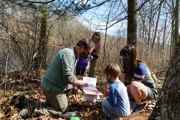 People gathered around a journal while in the woods