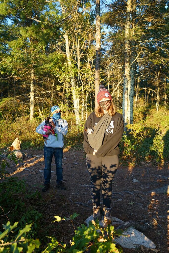 Two people holding small dogs pose for a picture while hiking