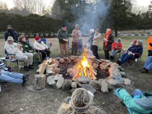 people sit around a large stone fire pit celebrating the winter solstice.